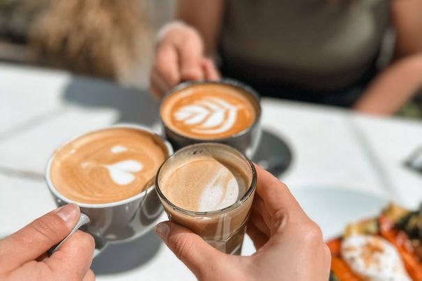 Tres personas brindan con cafés sobre una mesa con tostas.