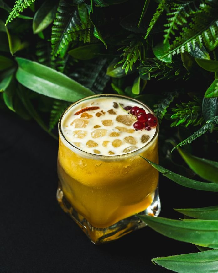 Cóctel de maracuyá con espuma, delante de hojas verdes.
