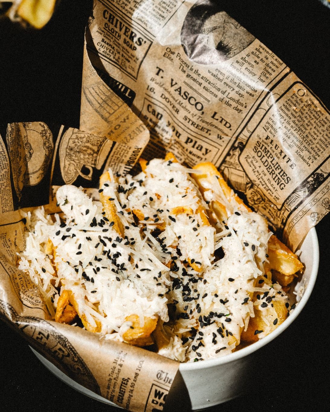 Patatas fritas con queso parmesano rallado y sésamo negro en un cubilete de papel.