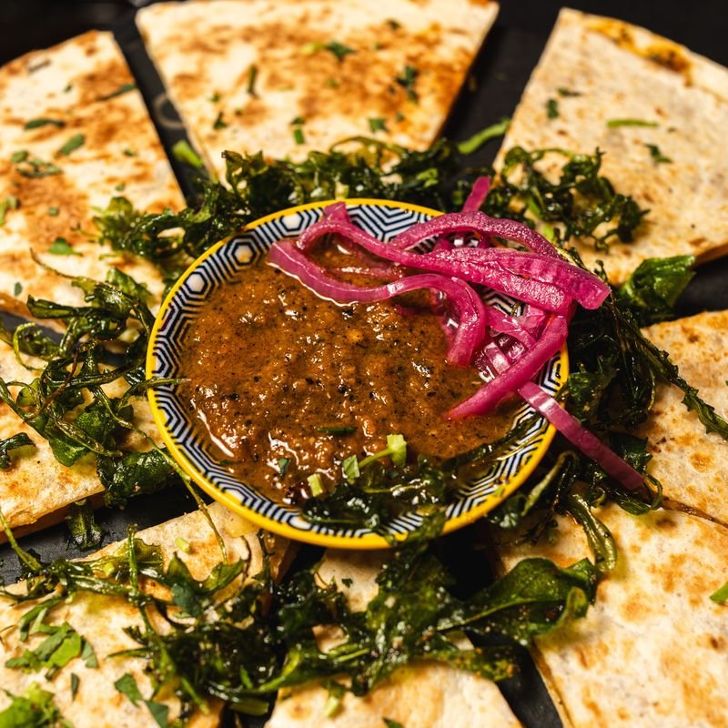 Quesadilla cortada en ocho porciones alrededor de un cuenco de birria con cebolla morada.
